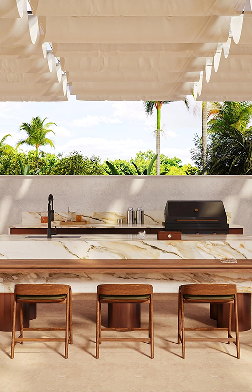 Outdoor kitchen with marble island, wooden stools, grill, sink, and tropical greenery background.