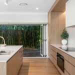 5144 Rossa Nova-Kristy Bunker project - Modern kitchen with wooden cabinetry, white countertops, built-in oven, induction cooktop, and open sliding doors.