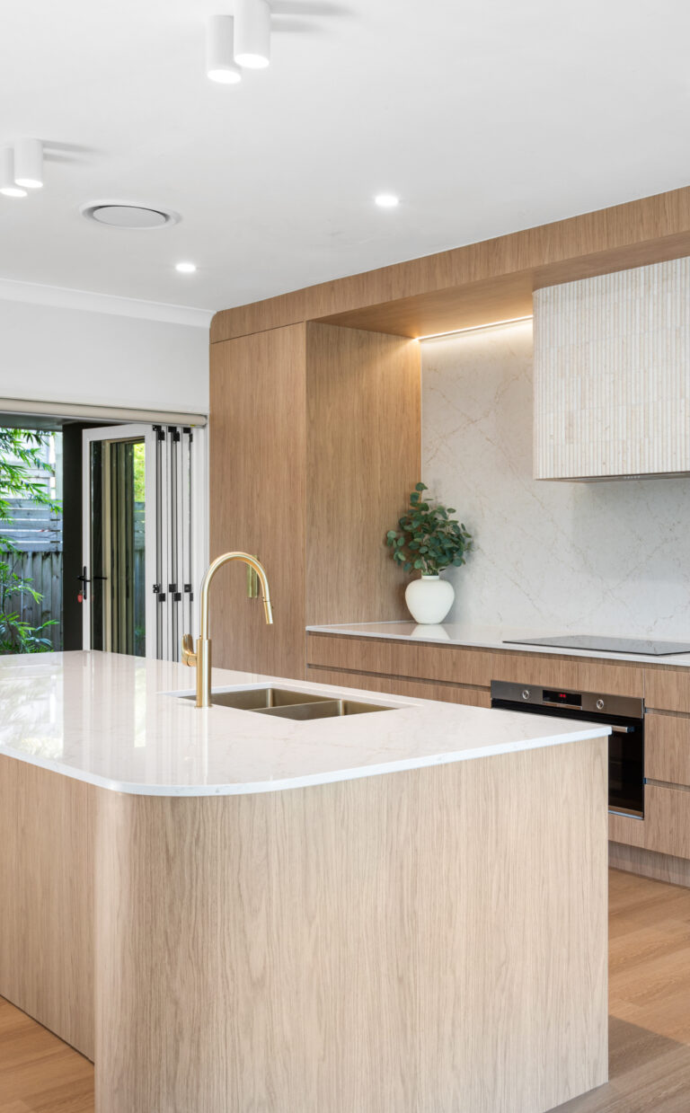 5144 Rossa Nova-Kristy Bunker project - Modern kitchen featuring a large island, wooden cabinetry, white countertops, built-in oven, and open sliding door.