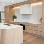 5144 Rossa Nova-Kristy Bunker project - Modern kitchen featuring a large island, wooden cabinetry, white countertops, built-in oven, and open sliding door.