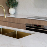 5144 Rossa Nova-Kristy Bunker project - Modern kitchen with brass faucet, double sink, wooden cabinets, built-in oven, and decorative plant.