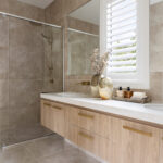 Caesarstone 5144 Rossa Nova surfaces in Modern bathroom with dual sinks, wooden cabinets, large mirror, glass shower, and decorative vases.