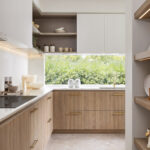 Caesarstone 5144 Rossa Nova surfaces in Modern kitchen with wooden cabinets, white countertops, open shelving, large window, and small appliances.