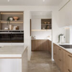 Caesarstone 5144 Rossa Nova surfaces in Modern kitchen with white countertops, wooden cabinetry, stainless steel appliances, large window, and pendant light.