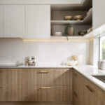 Caesarstone 5144 Rossa Nova surfaces in Modern kitchen with wooden lower cabinets, white upper cabinets, gold faucet, and large window.