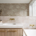 Caesarstone 5144 Rossa Nova surfaces in Modern bathroom with wooden vanity, white sink, bathtub, large mirror, and decorative dried flowers.