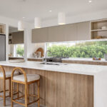 Carlisle Homes Illawarra Grand Theatre Atrium 44 Ridgelea in Modern kitchen with wooden accents, island seating, large window, built-in appliances, and pendant lighting.